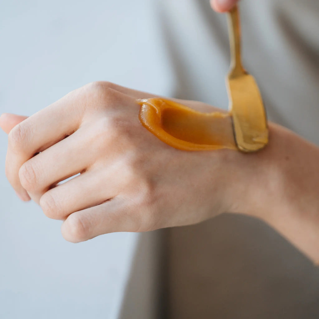Mānuka honey being spread on the back of a hand with a wooden spoon