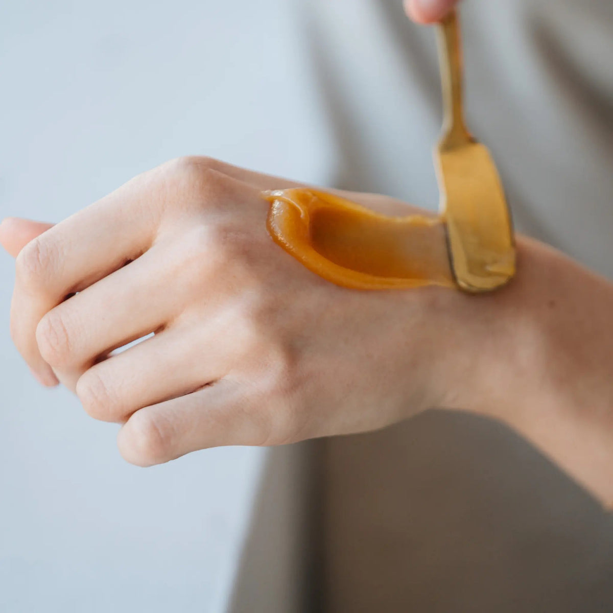 Mānuka honey being spread on the back of a hand with a wooden spoon