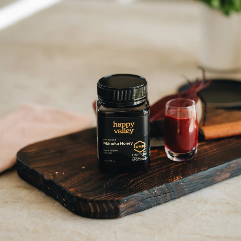 Happy Valley Mānuka Honey UMF 20+ jar on a wooden board with a drink