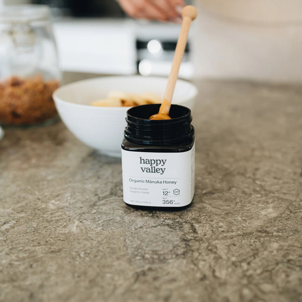 Happy Valley Organic Mānuka Honey jar with a wooden spoon