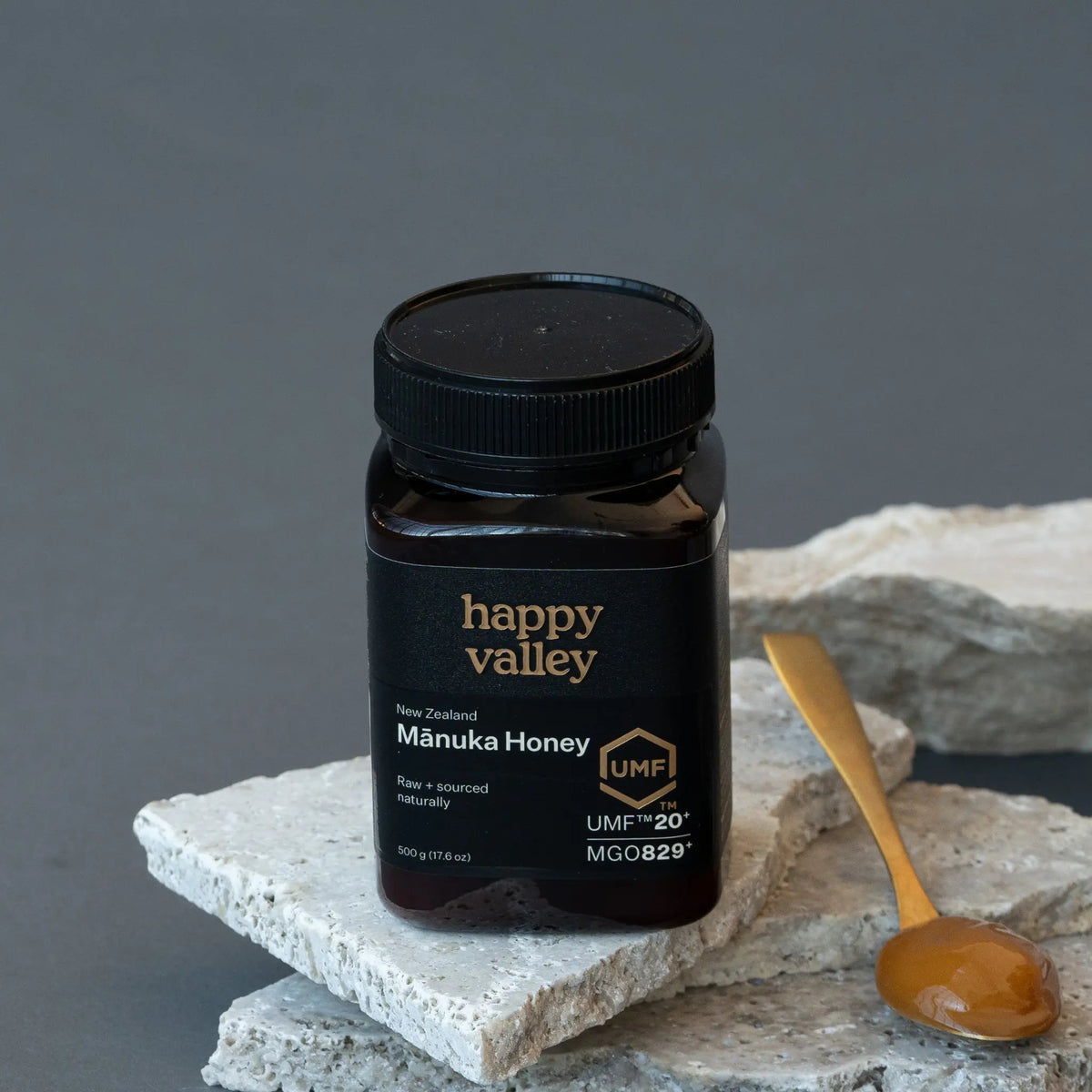 Happy Valley Mānuka Honey UMF 20+ jar on stone with a wooden spoon