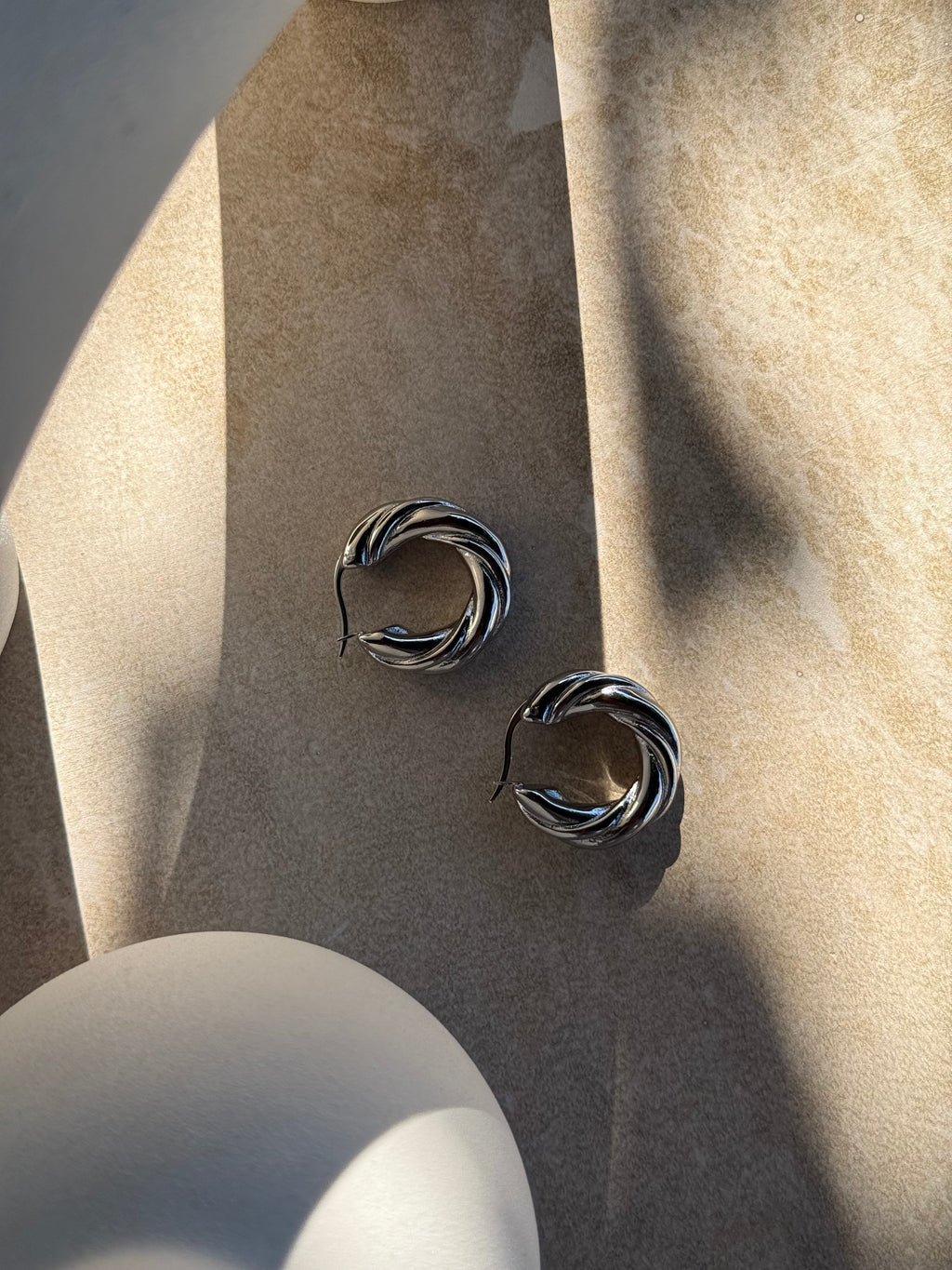 Tāwhirowhiro Silver Twisted Hoop Earrings on stone