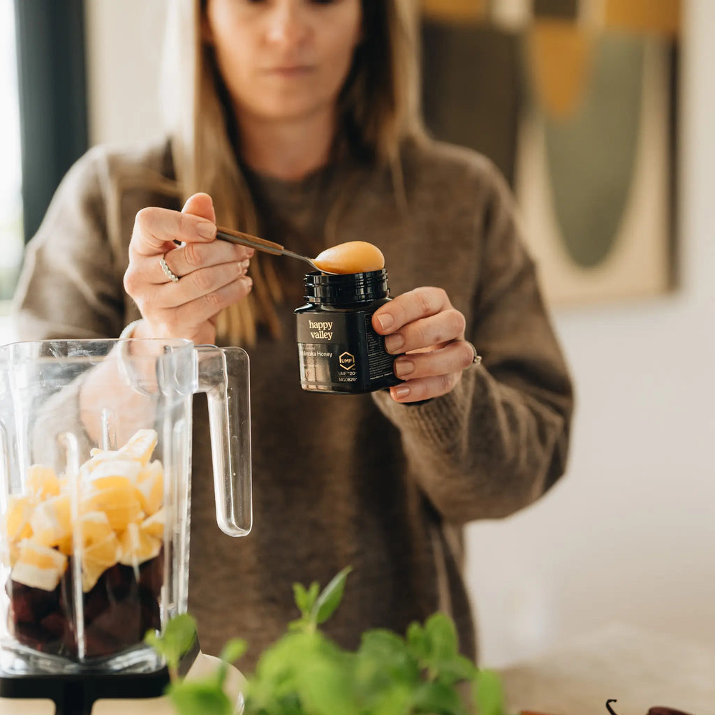 Person spooning Happy Valley Mānuka Honey into a blender