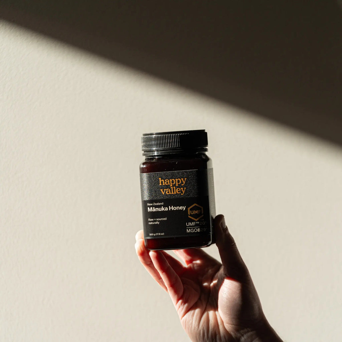 Hand holding up a jar of Happy Valley Mānuka Honey UMF 20+