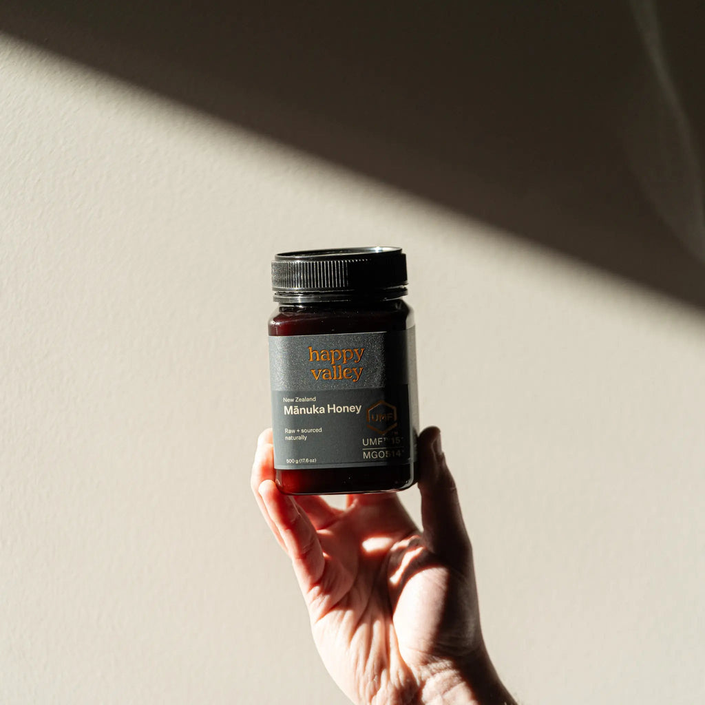 Hand holding up a jar of Happy Valley Mānuka Honey UMF 15+