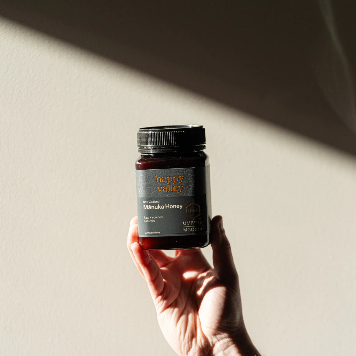 Hand holding up a jar of Happy Valley Mānuka Honey UMF 15+