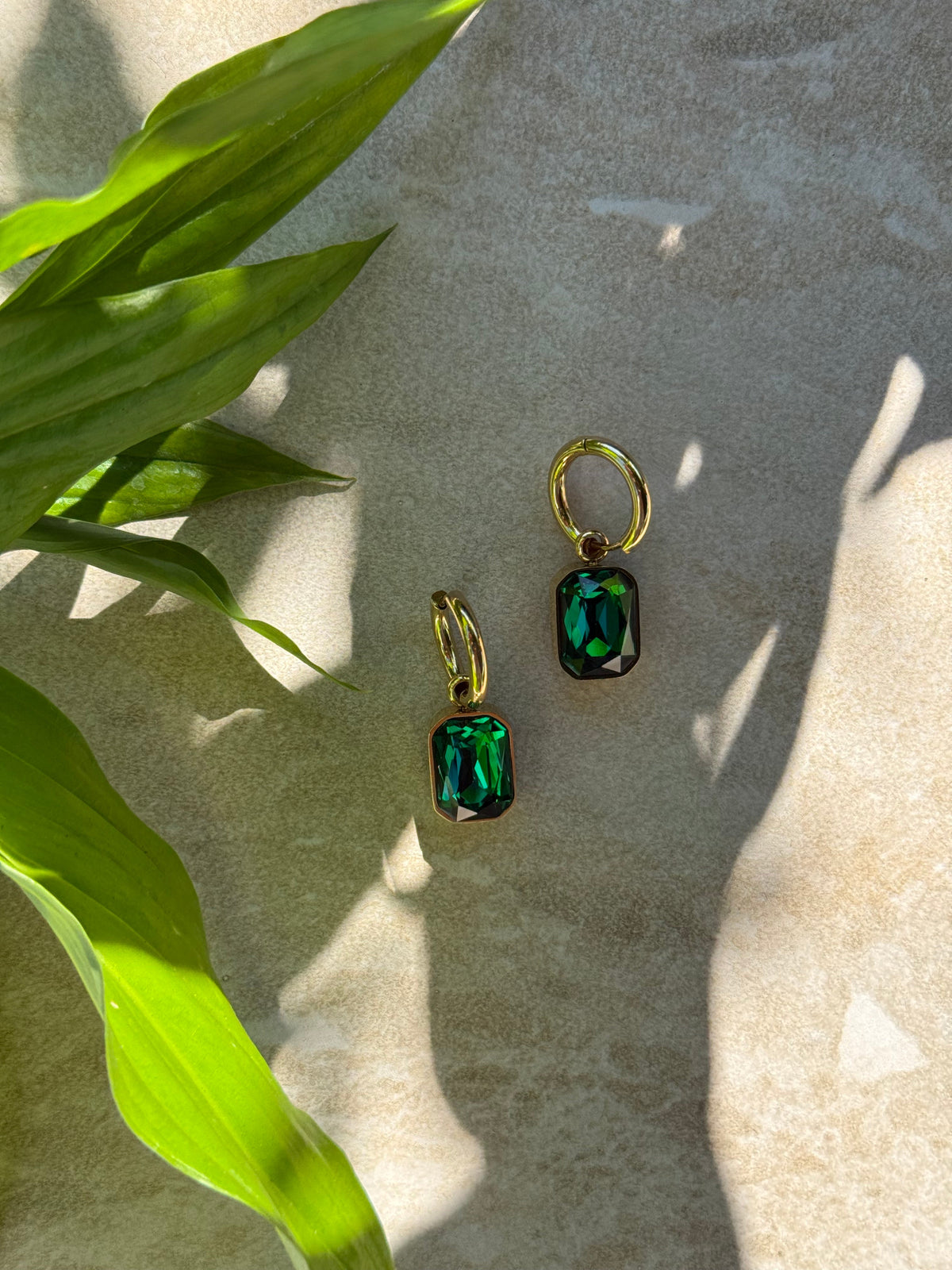 Taimana Kākāriki Gold Huggies with green stones, in dappled light