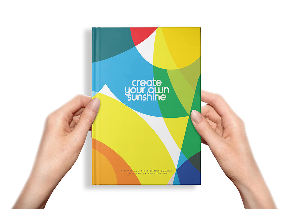 Hands holding a Resilient ME "Create Your Own Sunshine" journal