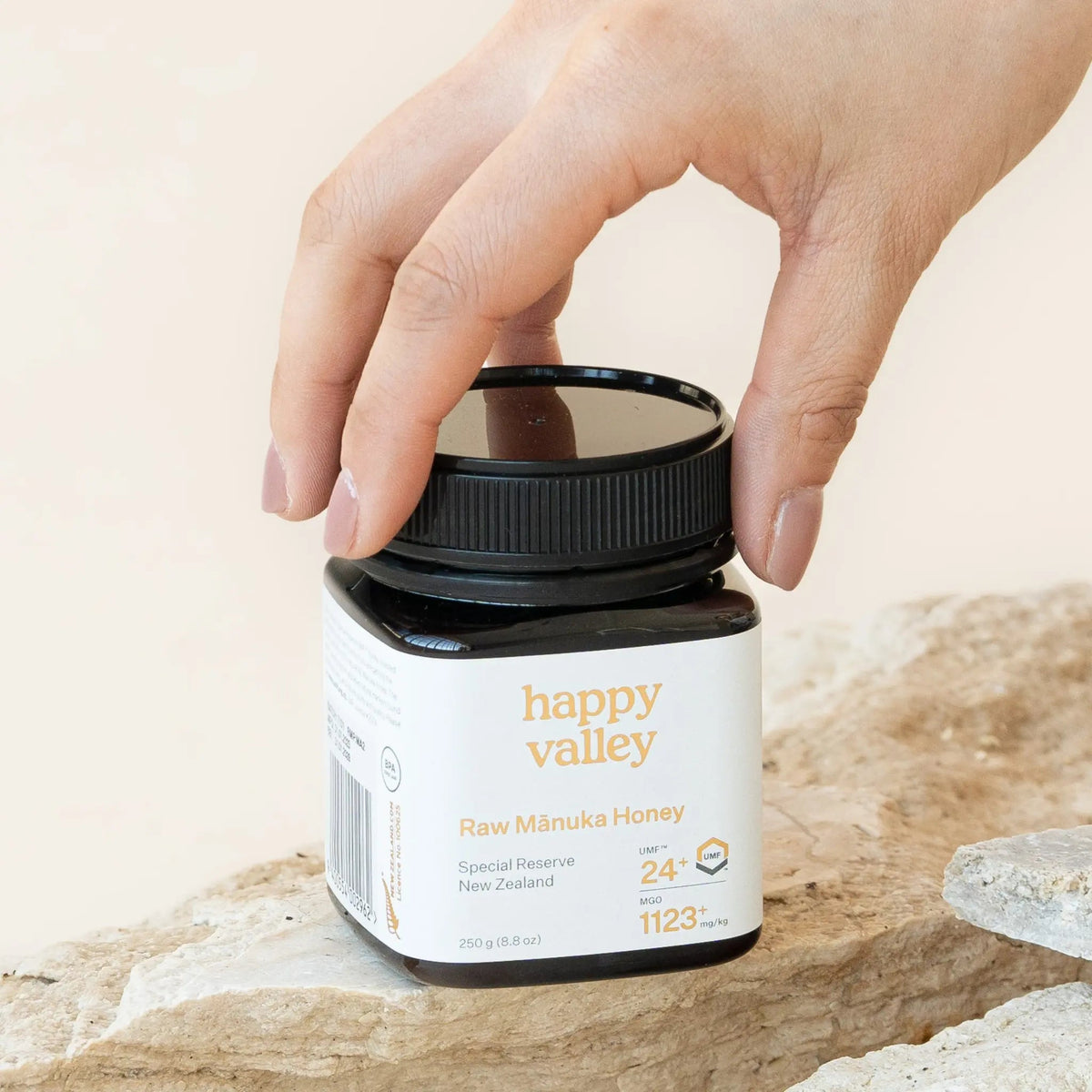 Hand lifting the lid of a Happy Valley Mānuka Honey UMF 24+ jar