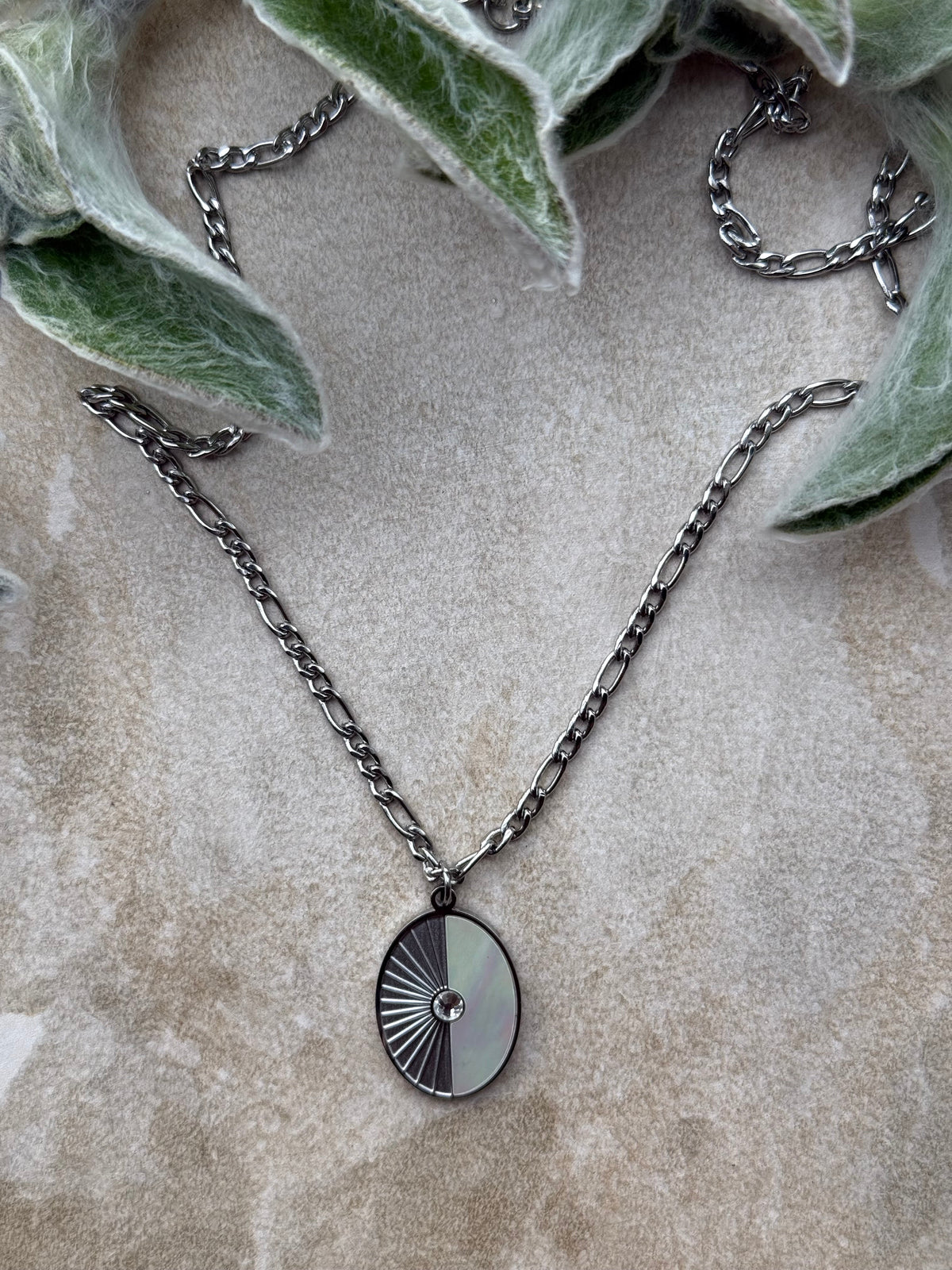 Pāua Whetū Silver Necklace on a stone with leaves