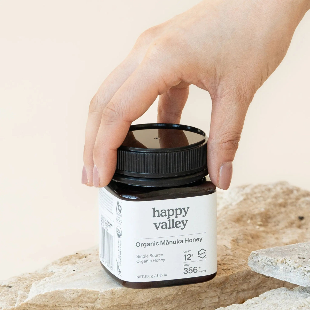 Hand lifting the lid of a Happy Valley Organic Mānuka Honey UMF 12+ jar