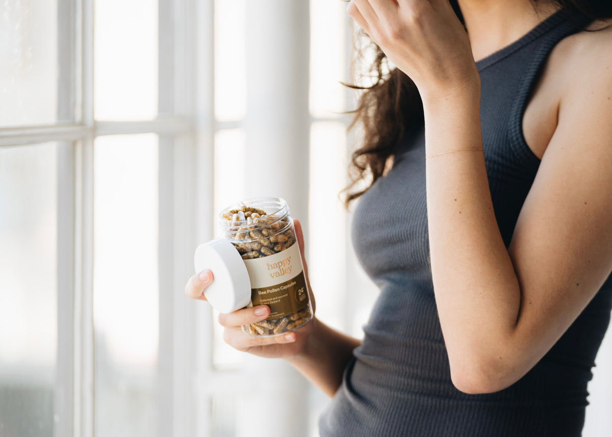 Person holding a jar of Happy Valley Bee Pollen Capsules by a window
