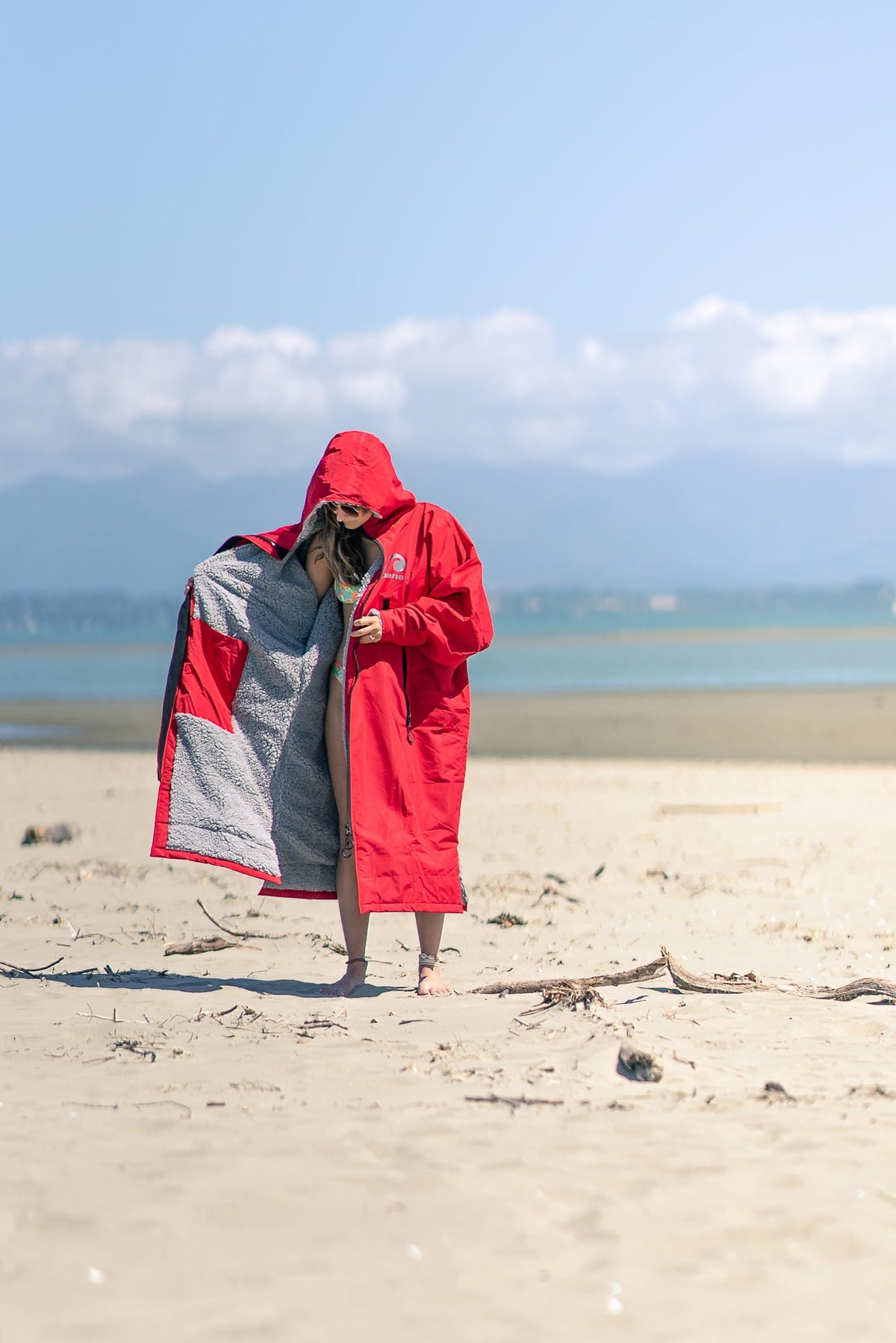Person on a beach holding open a red Moana SUP and Surf change robe to show the grey lining