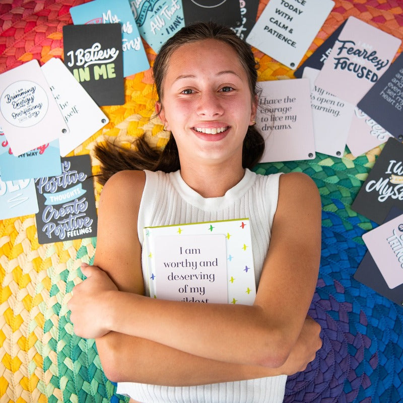 Smiling girl holding a Positive Affirmations card surrounded by cards