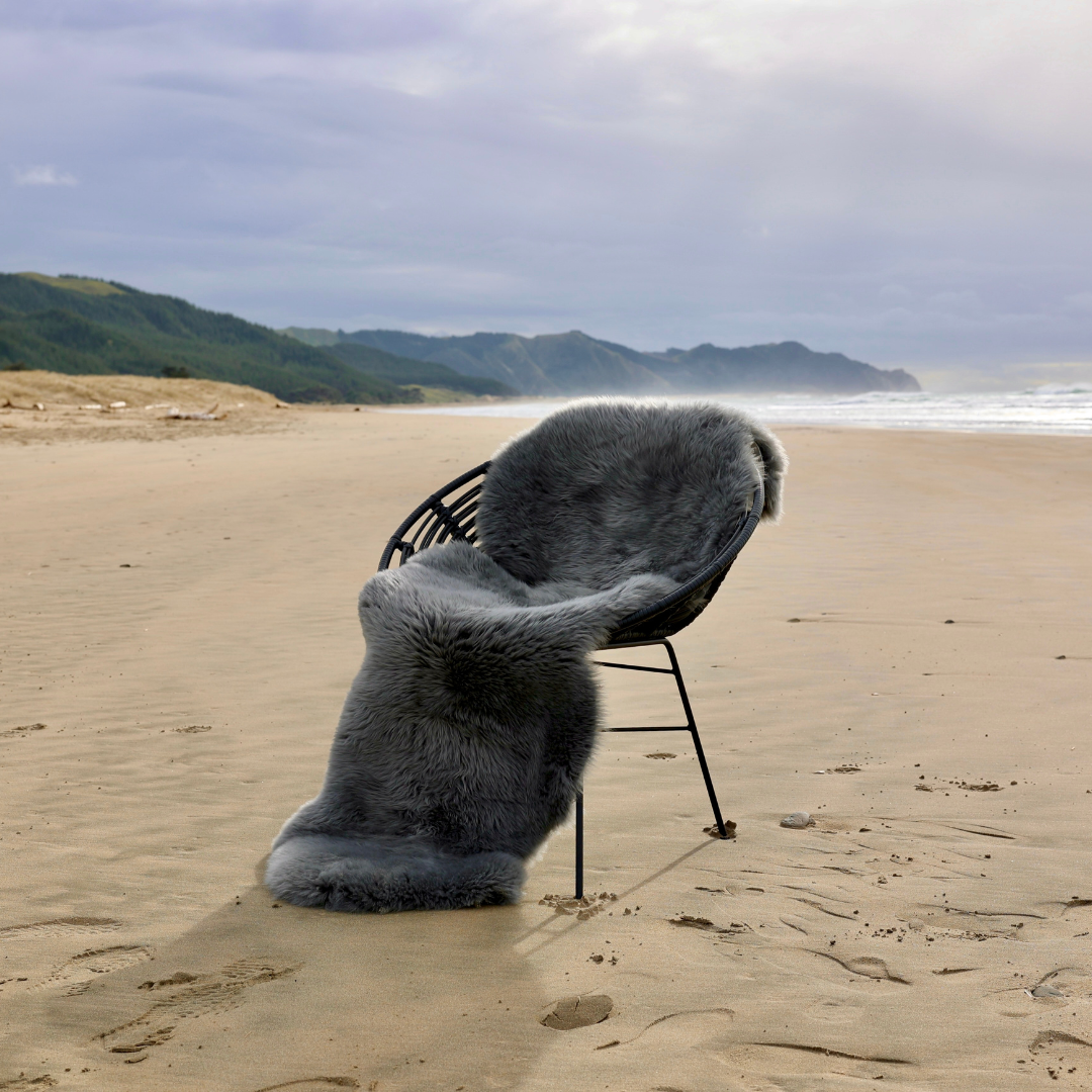 Grey double sheepskin rug draped over a chair on a beach