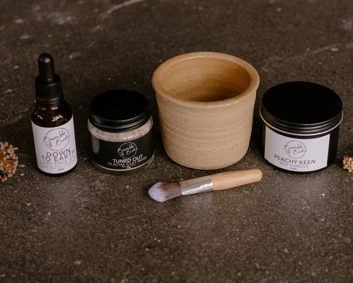 Down to Earth Ritual Set laid out: face oil, Tuned Out clay mask, clay bowl, mask brush and tin candle