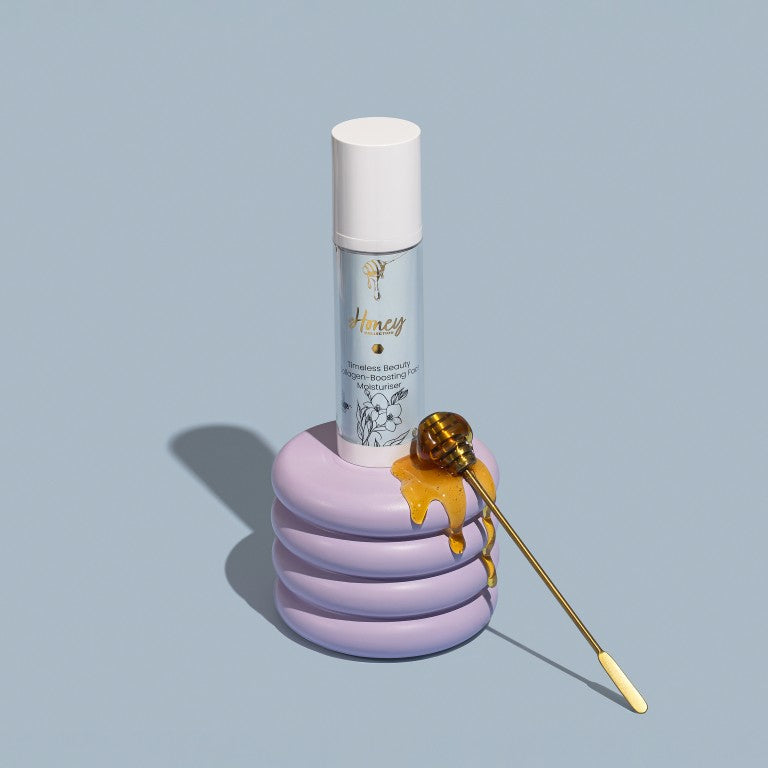 The Honey Collection face moisturiser bottle on a lilac stand with a honey dipper