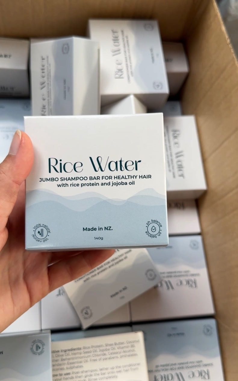 Hand holding a NaturalCare Rice Water box above a carton of boxes