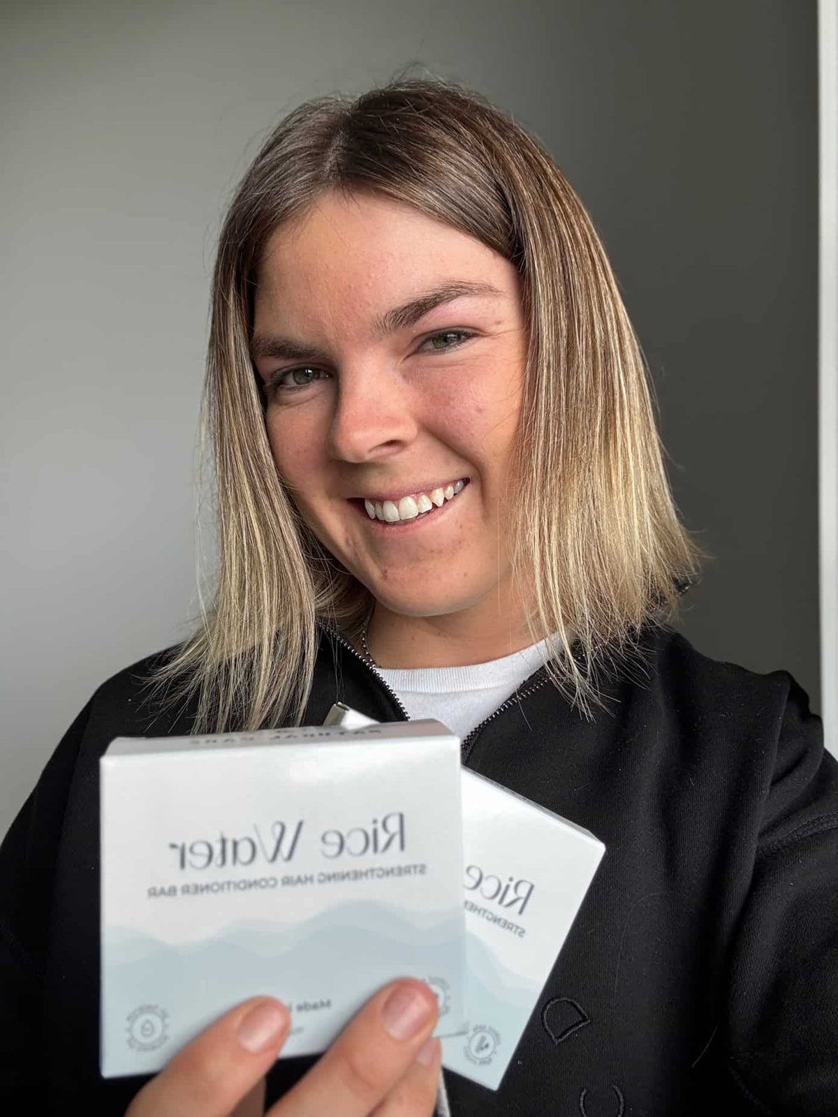 Smiling woman holding NaturalCare Rice Water boxes
