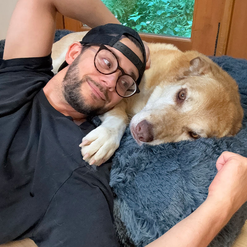 Man lying beside an older dog on a dark grey Brooklyn Ultra memory foam dog bed