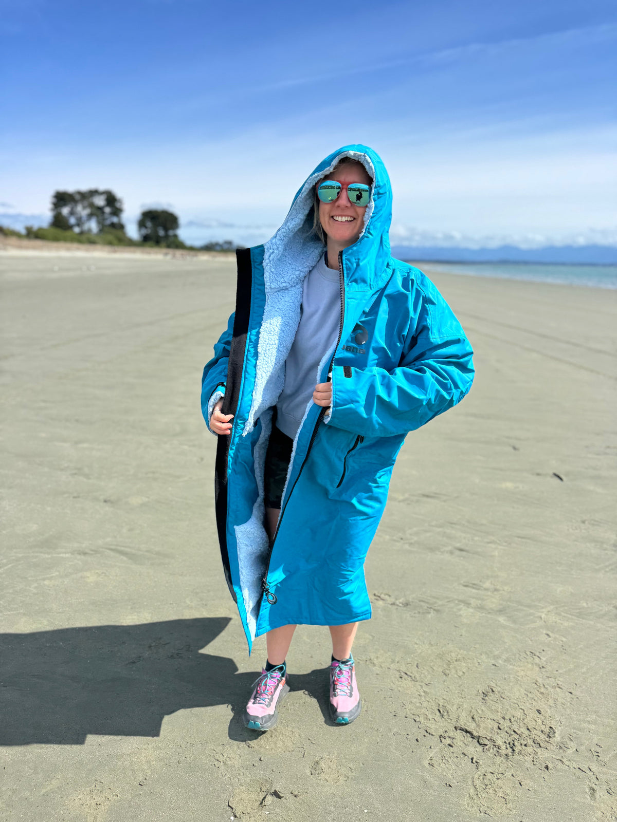 Woman on a beach holding open an ocean blue Moana SUP and Surf change robe to show the lining
