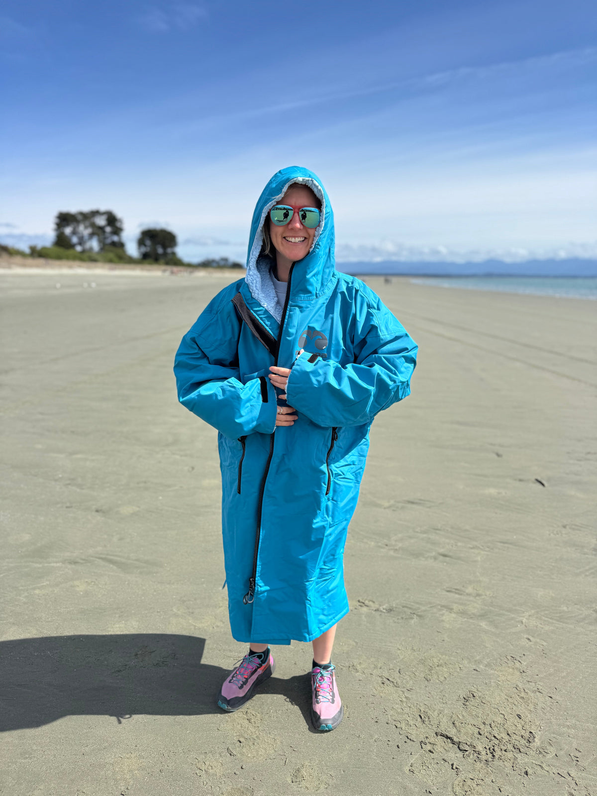 Woman on a beach in an ocean blue Moana SUP and Surf change robe, hood up