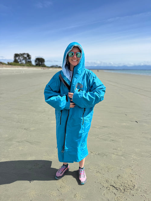 Woman on a beach in an ocean blue Moana SUP and Surf change robe, hood up