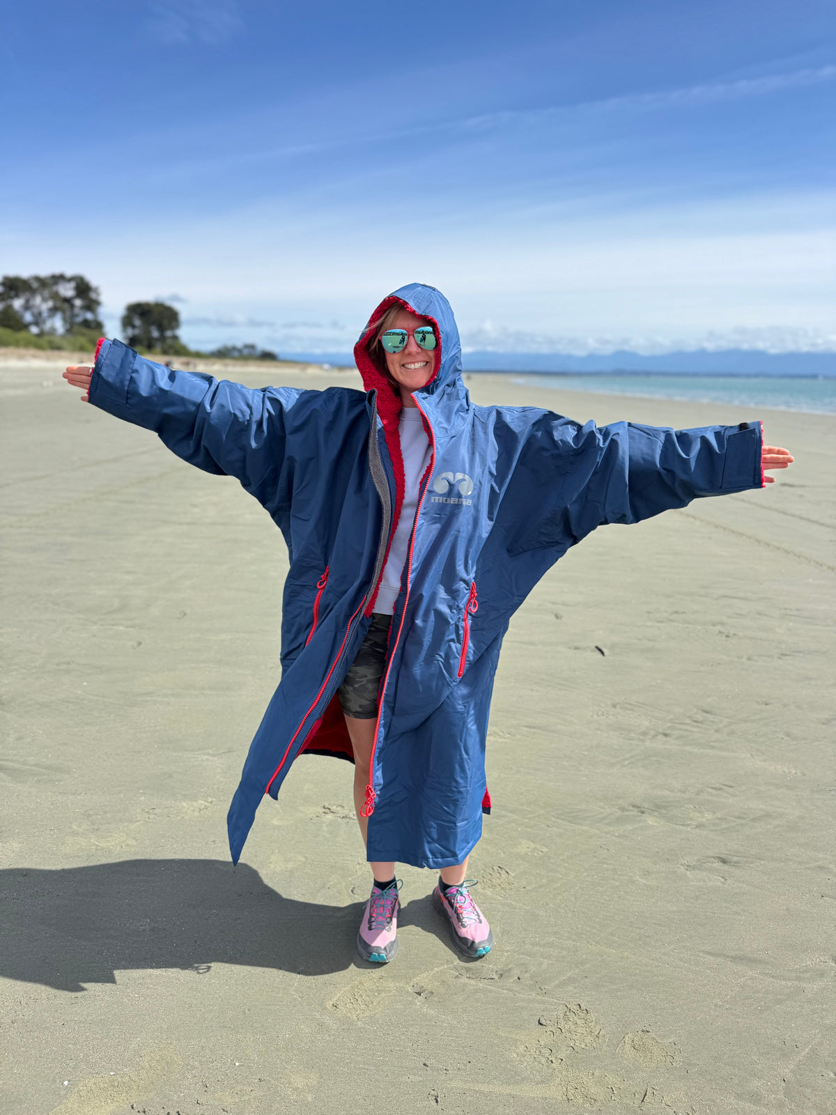 Woman on a beach wearing a navy and red Moana SUP and Surf change robe, arms outstretched