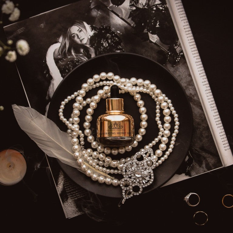 Honey Face Serum bottle on a black plate with pearls