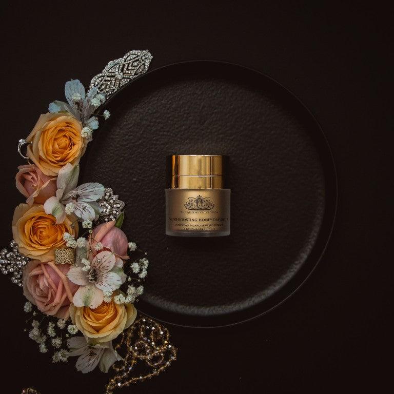 The Honey Collection day cream jar on a black plate with flowers