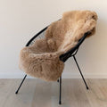 Sand 1.5 sheepskin rug draped over a black chair