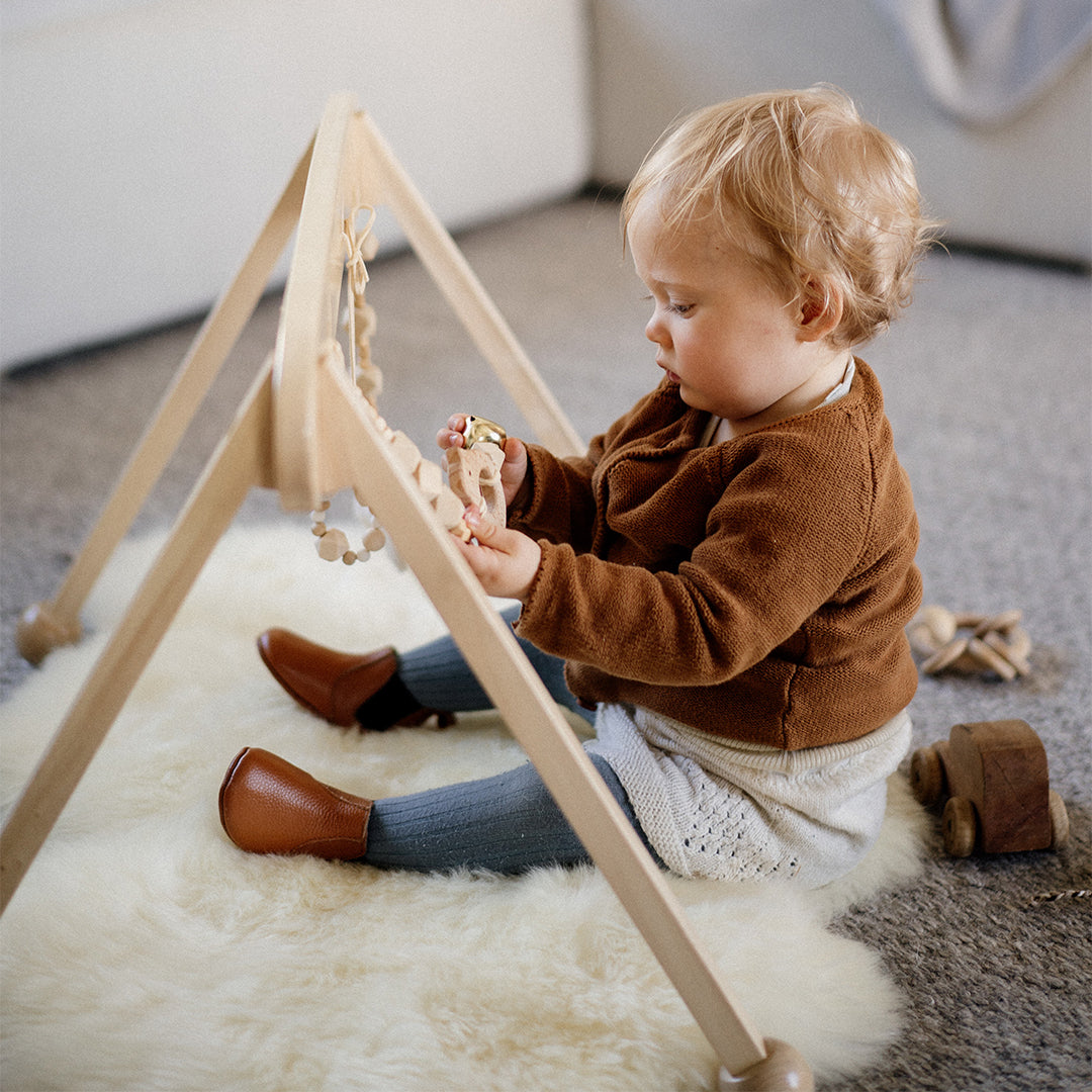 Toddler playing under a wooden play gym on a sheepskin baby rug
