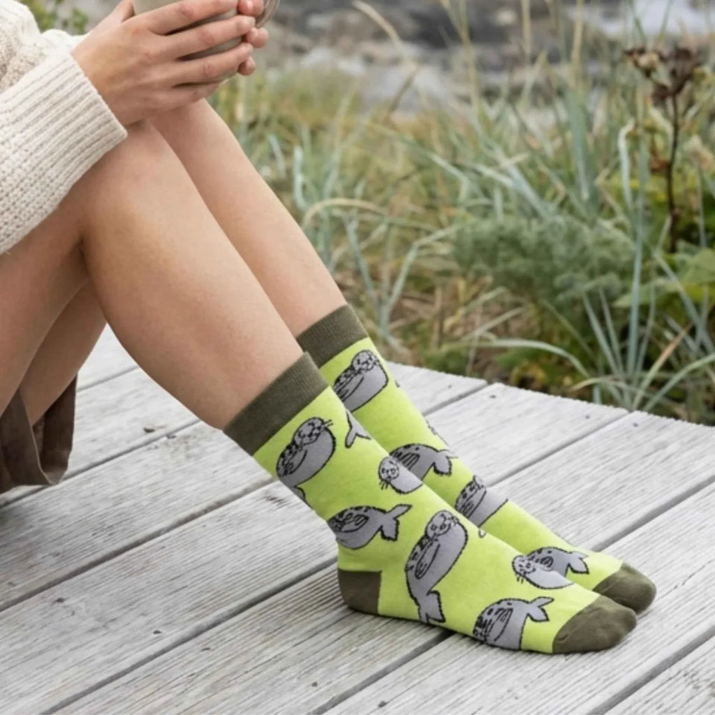 Person sitting on a deck wearing green Barekind seal socks
