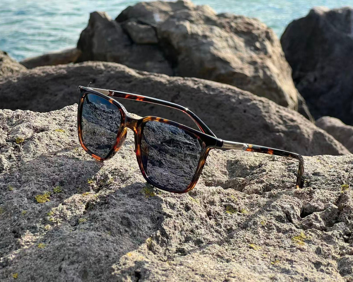 URBA VISTA Azure tortoiseshell sunglasses resting on a rock by the sea