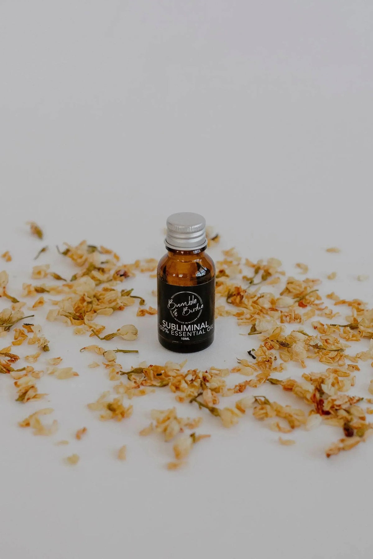 Subliminal essential oil blend in a small amber bottle by Bumble & Birdie, among dried petals