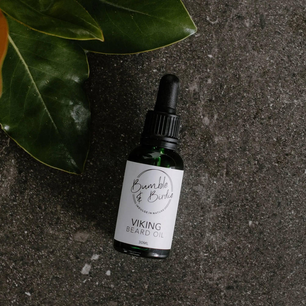 Viking beard oil in a dropper bottle by Bumble & Birdie, on dark stone with leaves