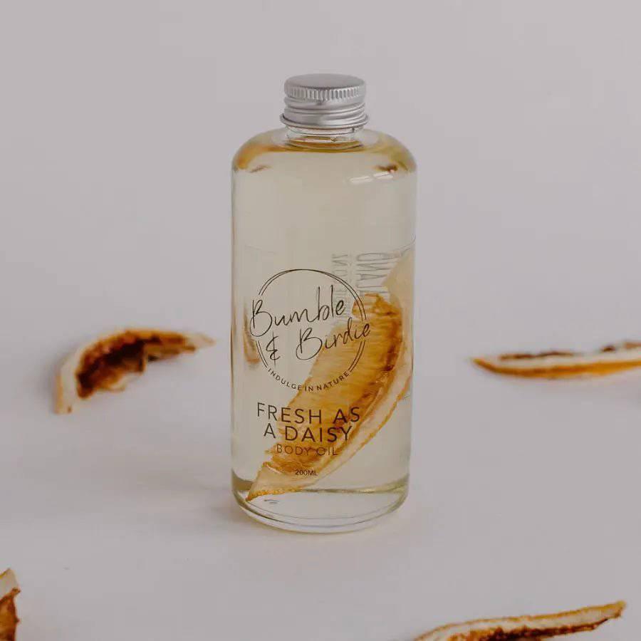 Fresh as a Daisy bath and body oil in a clear bottle by Bumble & Birdie, with dried citrus slices
