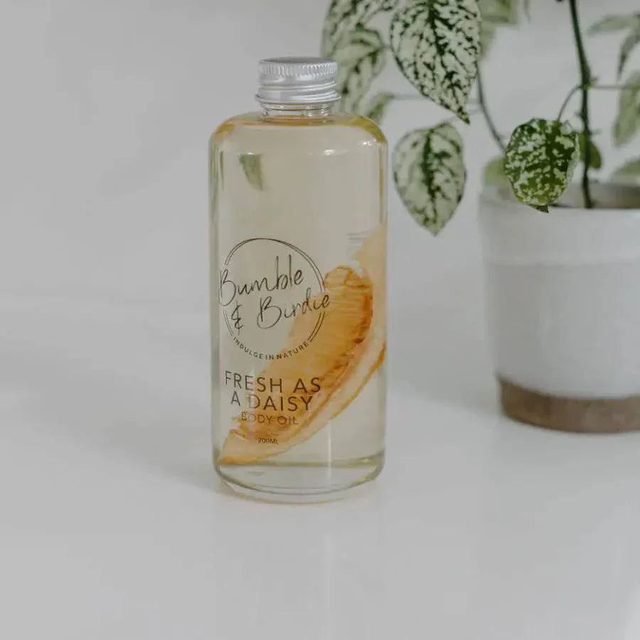 Fresh as a Daisy bath and body oil bottle beside a potted plant