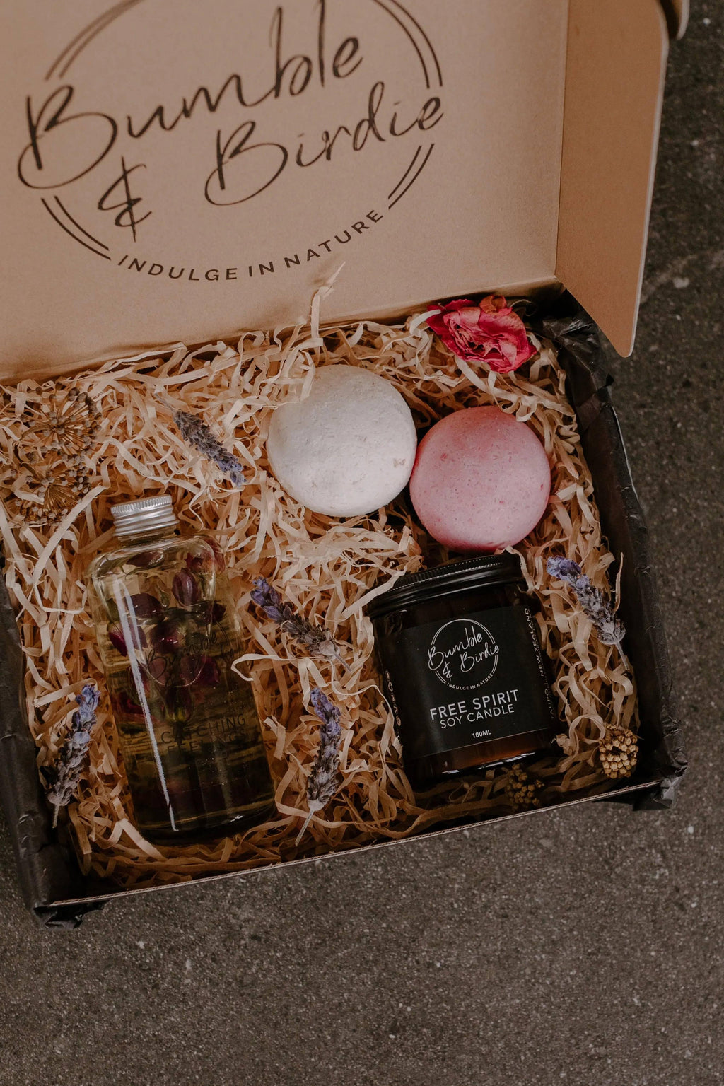 Kiss & Tell Gift Set in an open Bumble & Birdie box with a body oil, jar candle and two bath bombs