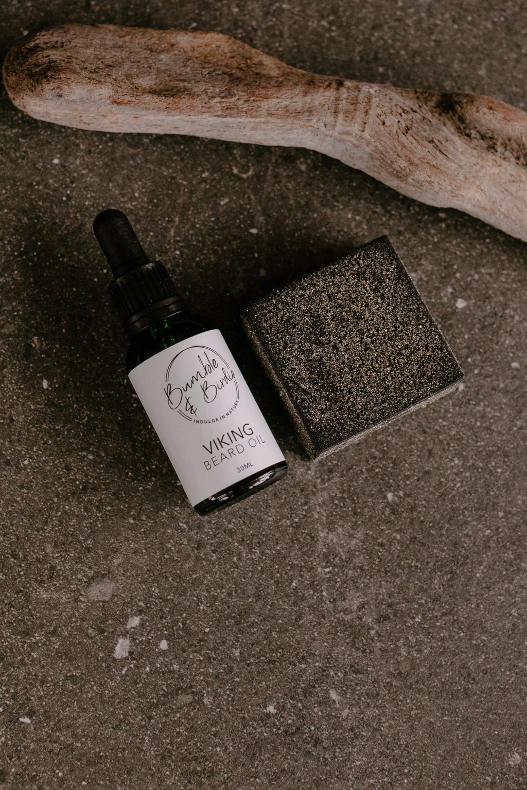 Viking beard oil and a black clay shaving bar from the Elixir Master Beard set, with driftwood