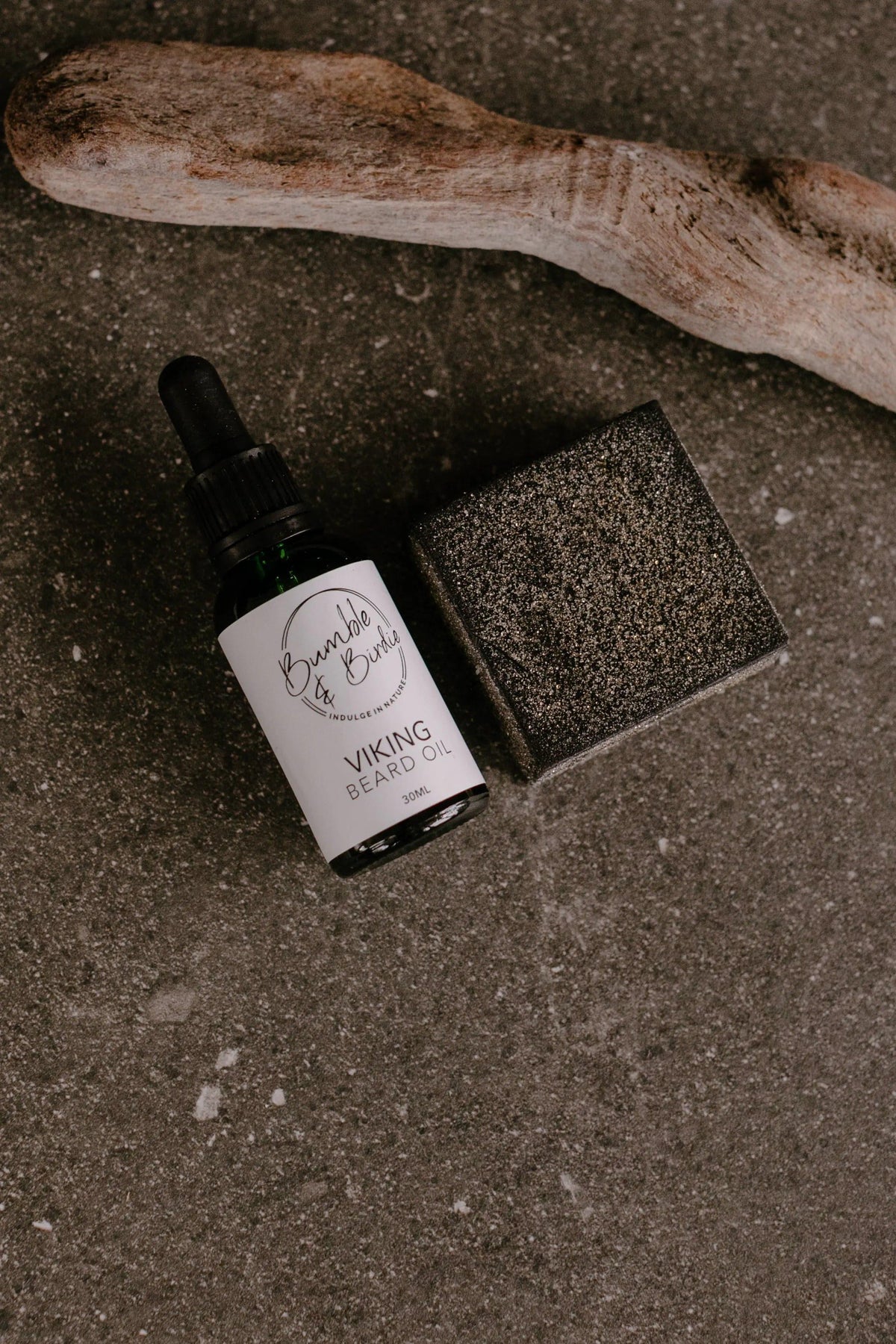 Viking beard oil and a black clay shaving bar from the Elixir Master Beard set, with driftwood