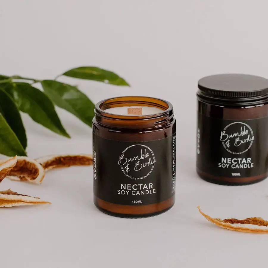 Two Nectar soy jar candles, one open with a wood wick, with leaves and dried orange