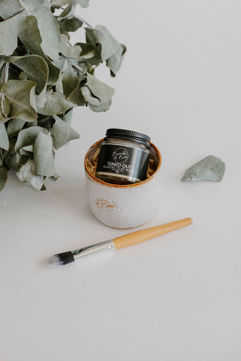 Clay Mask Ritual Set with a clay mask jar, a speckled clay pot and a mini mask brush beside eucalyptus