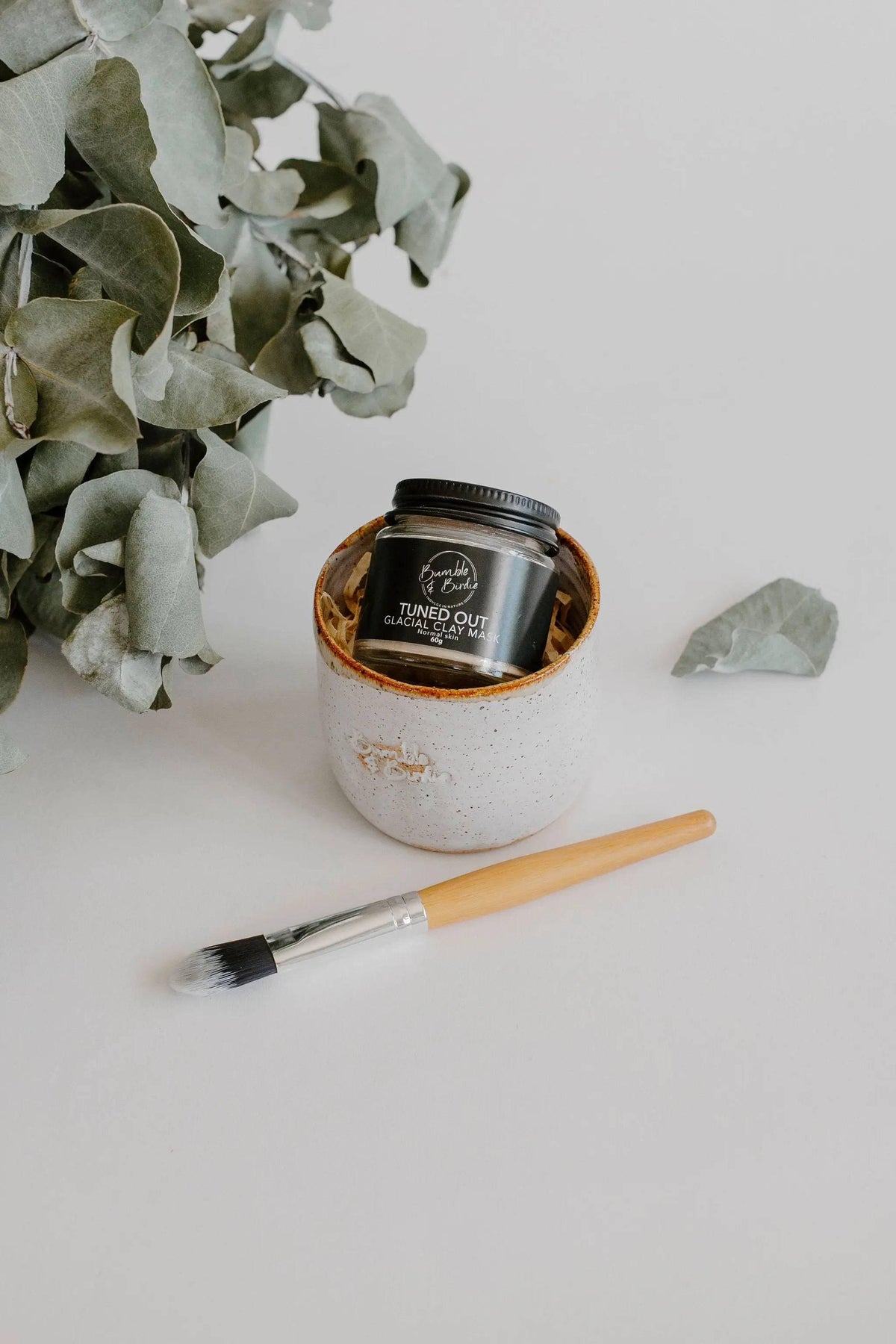 Clay Mask Ritual Set with a clay mask jar, a speckled clay pot and a mini mask brush beside eucalyptus