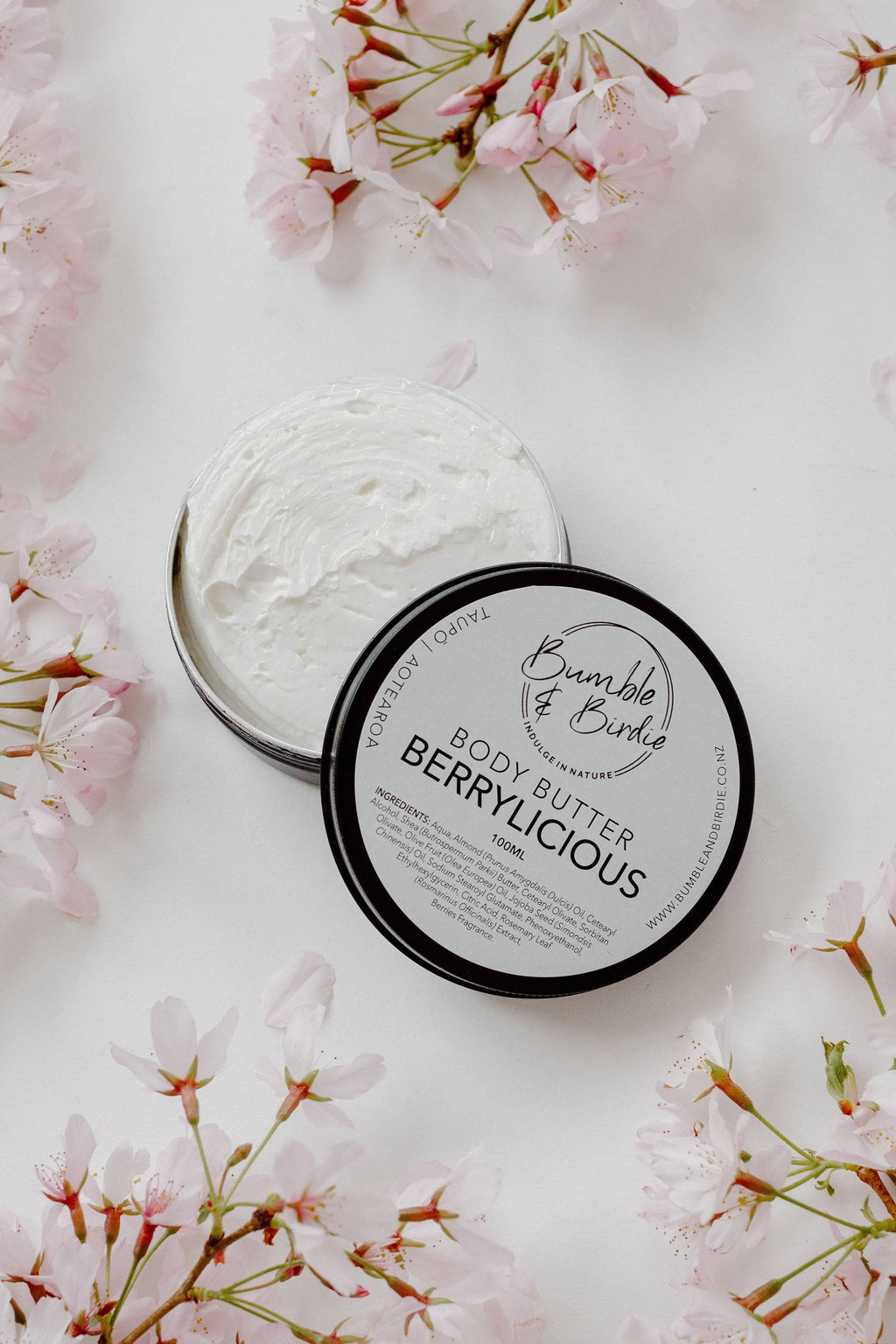 Open tin of Berrylicious body butter showing the whipped texture, with pink blossom