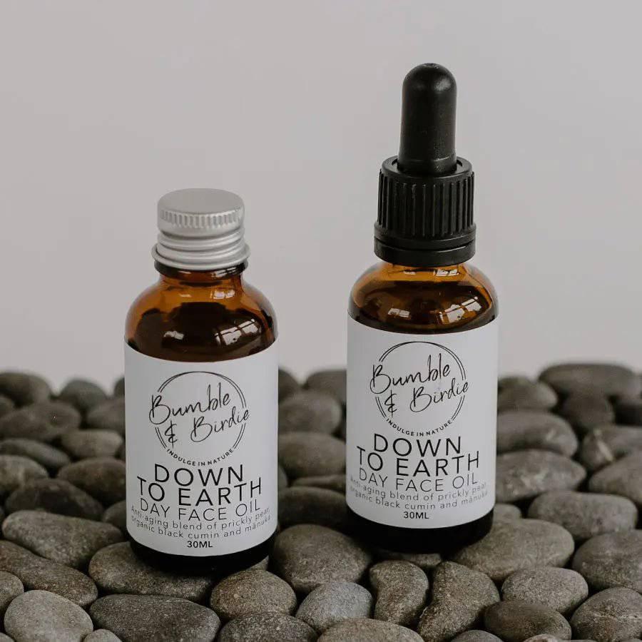 Down to Earth day face oil in a refill bottle and a dropper bottle by Bumble & Birdie, on grey pebbles