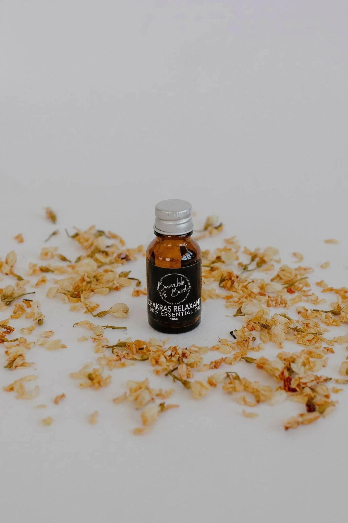Chakras Relaxant essential oil blend in a small amber bottle by Bumble & Birdie, among dried petals