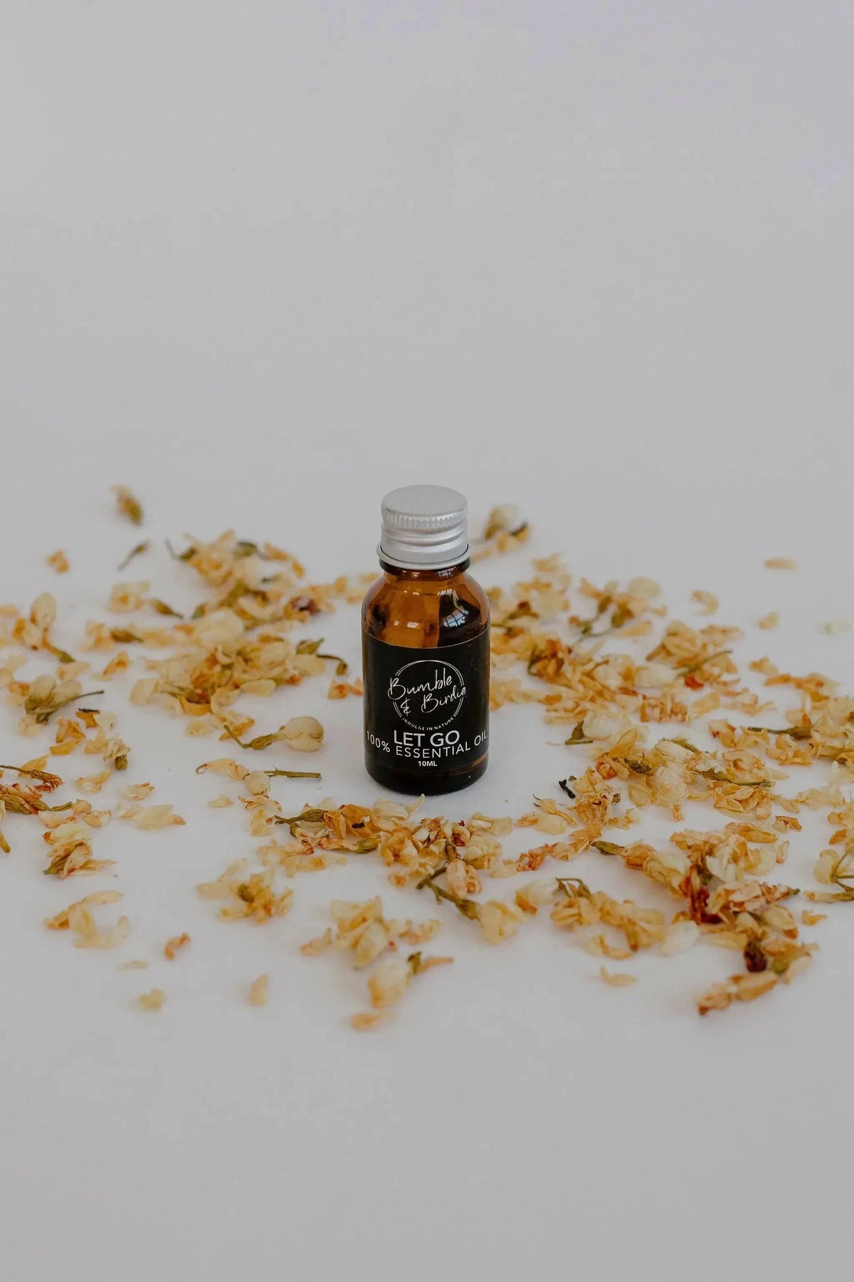 Let Go essential oil blend in a small amber bottle by Bumble & Birdie, among dried petals