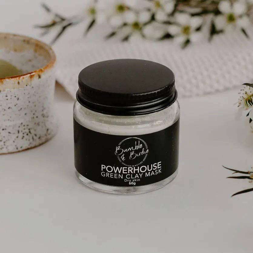 Jar of Powerhouse Green Clay Mask by Bumble & Birdie beside a speckled clay bowl and white flowers
