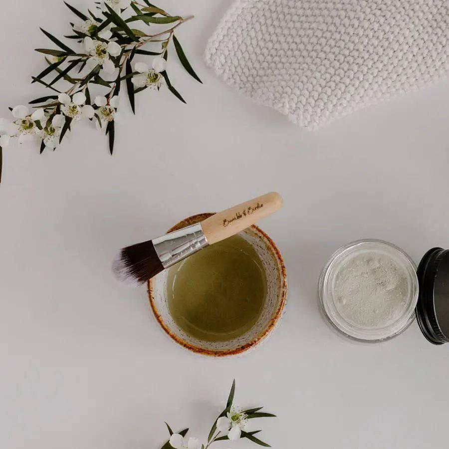 Powerhouse green clay mask mixed in a clay bowl, with a mask brush and the open jar of powder
